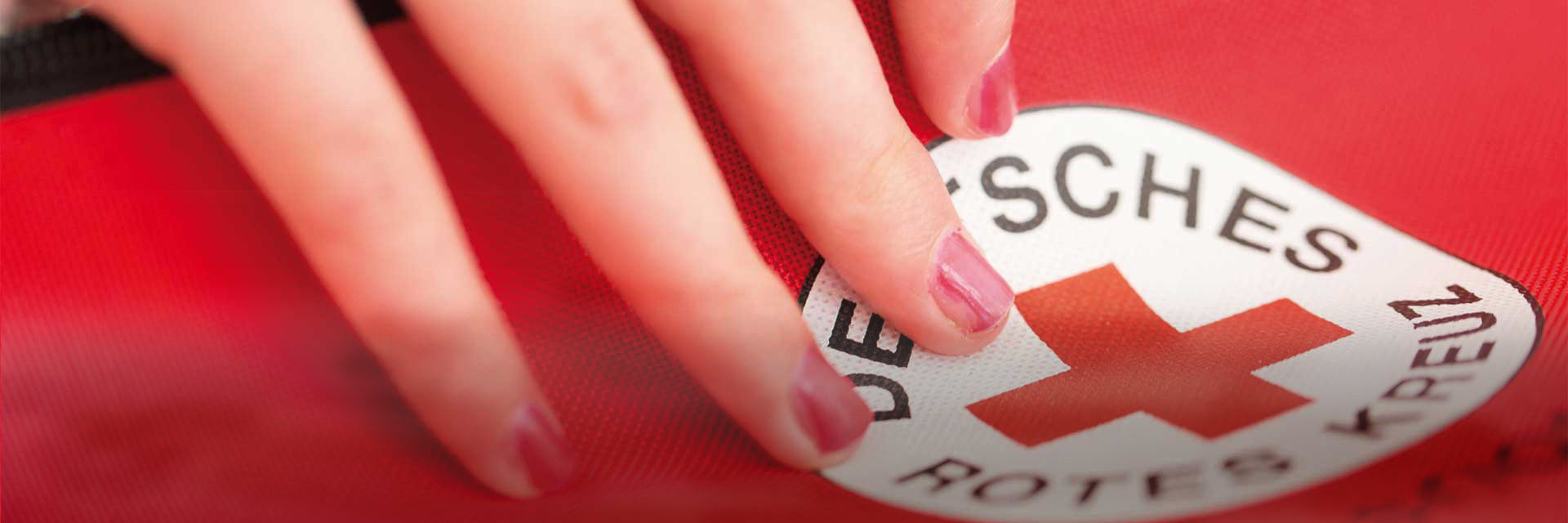 Hand klebt DRK Rundlogo auf roten Untergrund
