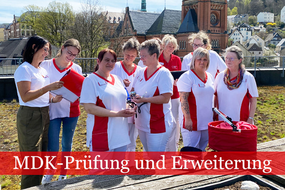 Team des ambulanten Pflegedienstes in rot-weißer Dienstkleidung stehen auf der Dachterrasse und sind in ein Gespräch vertieft.