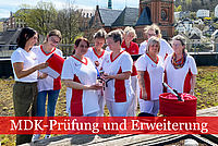Team des ambulanten Pflegedienstes in rot-weißer Dienstkleidung stehen auf der Dachterrasse und sind in ein Gespräch vertieft.