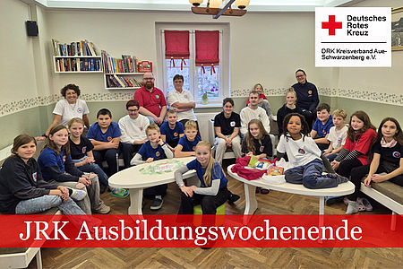 JRK Ausbildungswochenende: Gruppenfoto im Aufenthaltsraum, alle Teilnehmer sitzen im Raum verteilt auf Tischen und Stühlen.