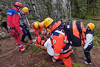 Fortbildung der Bergwacht: Bergwachtmitglieder betreuen einen Patienten in der Schleifkorbtrage, im Vordergrund eine Einsatzkraft mit Einsatzrucksack
