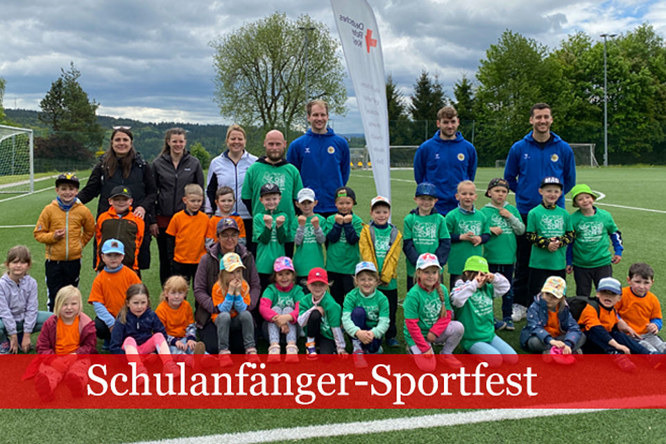 660_2026_Schulanfänger_Sportfest_3.jpg Schulanfänger-Sportfest: Gruppenfoto auf dem Sportplatz mit Kindergartenkindern und drei Sportlern des EHV Aue, in der Mitte eine DRK-Flagge