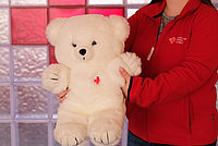 Junge Frau hält großen weißen Teddybär mit DRK-Logo
