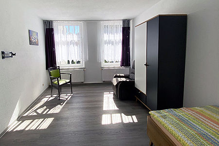 Blick in ein freies Bewohnerzimmer mit Fensterfront und vorhandener Ausstattung