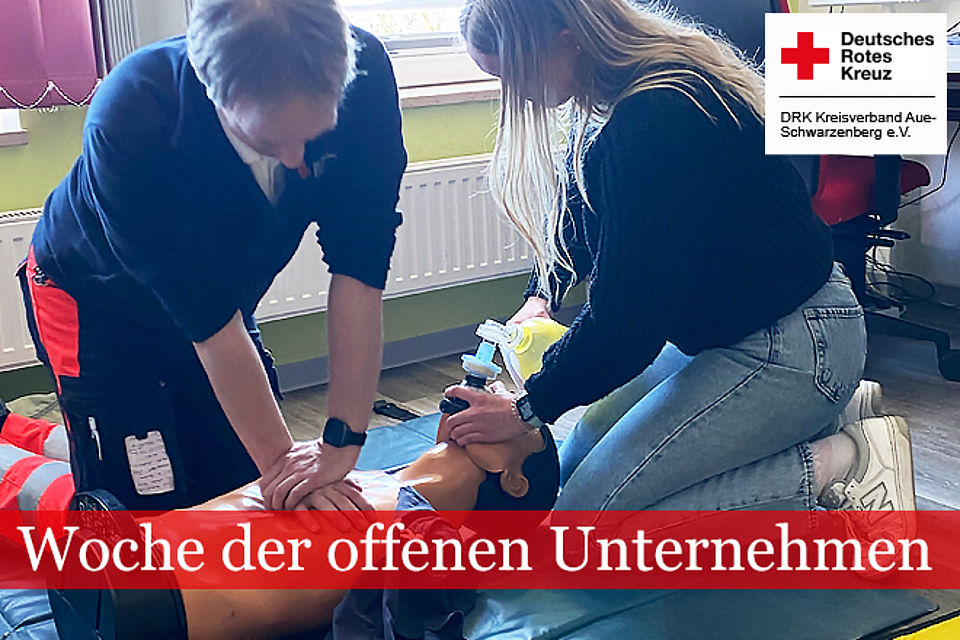 Praxisanleiter in DRK Kleidung erläutert einer Jugendlichen die Wiederbelebung an einer Übungspuppe
