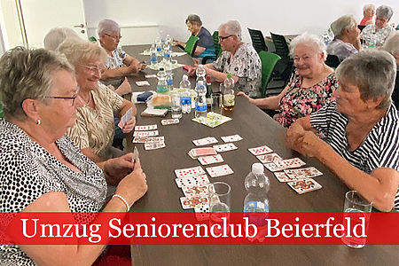Mehrere Seniorinnen sitzen an einem langen Tisch und spielen Karten.