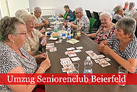 Mehrere Seniorinnen sitzen an einem langen Tisch und spielen Karten.