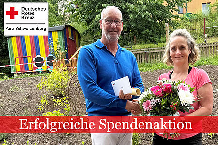 DRK Geschäftsführer Thomas Illert (links) überreicht Erzieherin Antje Beier einen Blumenstrauß und schüttelt ihr die Hand. Beide stehen im Garten der Kita, im Hintergrund ein bunter Bauwagen.