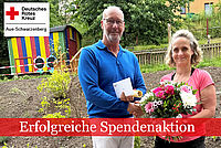 DRK Geschäftsführer Thomas Illert (links) überreicht Erzieherin Antje Beier einen Blumenstrauß und schüttelt ihr die Hand. Beide stehen im Garten der Kita, im Hintergrund ein bunter Bauwagen.