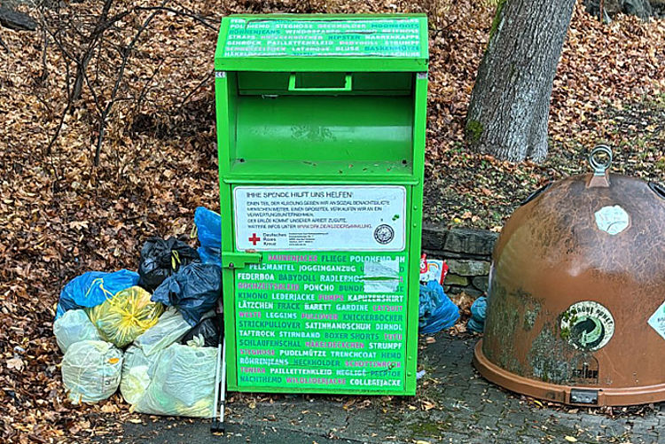 Grüner Altkleidercontainer des DRK mit zusätzlich abgelegten Müllsäcken daneben