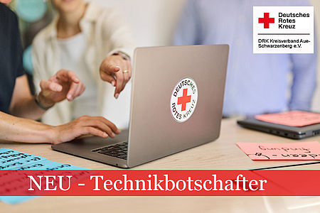 Laptop mit DRK-Logo steht auf einem Tisch. Mehrere Hände zeigen darauf.