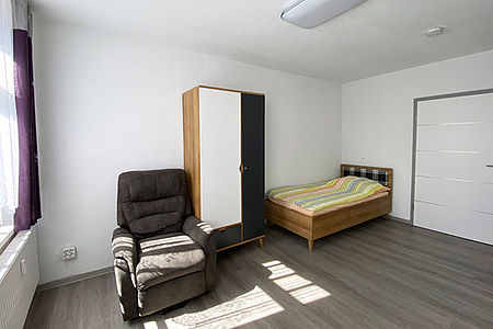 Freies Bewohnerzimmer mit Schrank, Sessel und Bett