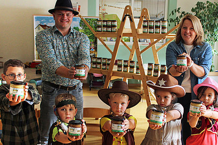 Zwei Erwachsene und fünf Kinder in Western-Kostümen strecken volle Honiggläser vor sich aus.