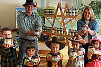 Zwei Erwachsene und fünf Kinder in Western-Kostümen strecken volle Honiggläser vor sich aus.