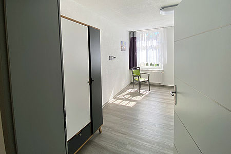 Blick in ein freies Bewohnerzimmer mit Schrank und Fensterfront