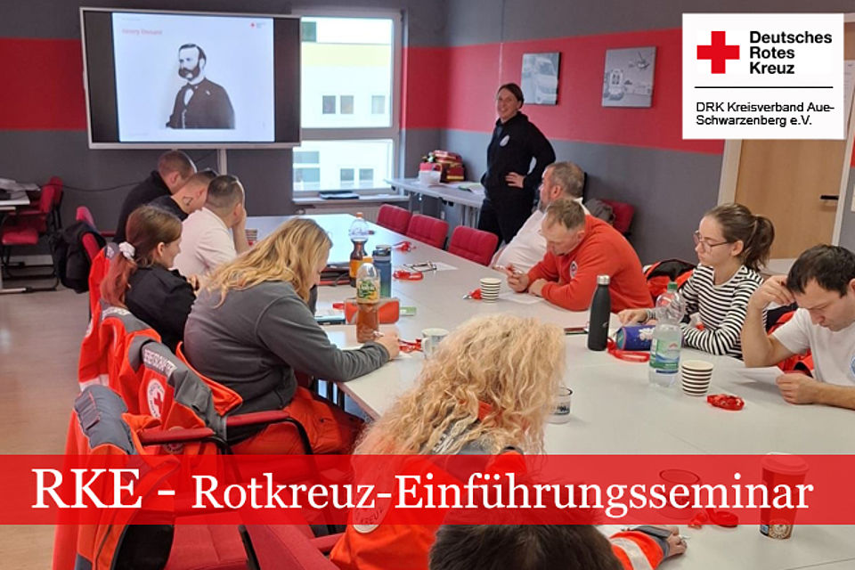 660_2025_RKE_1.jpg RKE-Rotkreuz-Einführungsseminar: Die Kursteilnehmer sitzen an einem langen Tisch. Die Ausbliderin in DRK Kleidung steht vorn und zeigt ein Portrait von Henry Dunant.