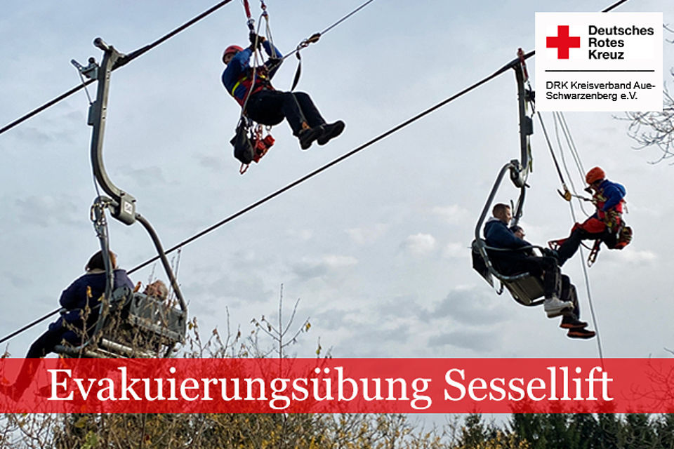 Retter in Bergwachtkleidung nähern sich an einem Sessellift den Personen, die im Lift festsitzen.