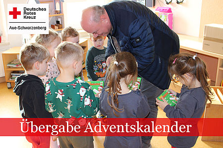 Übergabe Adventskalender: Im Gruppenraum der Kita beugt sich ein Mann zu den Kindern und verteilt die Adventskalender
