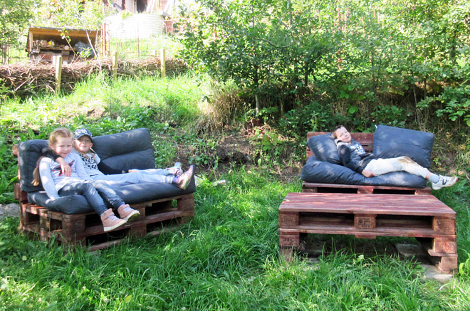 Zwei Palettensofas im Garten der Kita Pöhlbachzwerge, drei Kinder ruhen sich darauf aus
