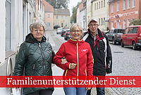 Familienunterstützender Dienst: Mitarbeiterin in DRK Kleidung geht mit einem älteren Ehepaar die Straße entlang. Die hält die Frau eingehenkelt.