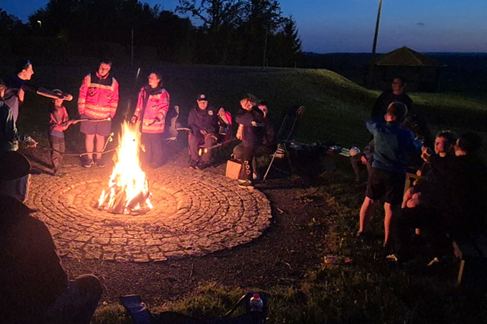Kinder und Jugendliche, einige davon in DRK-Kleidung sitzen um ein Lagerfeuer