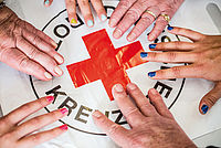 Symbolfoto: mehrere Hände mit bunt lackierten Fingernägeln über einem DRK-Rundlogo