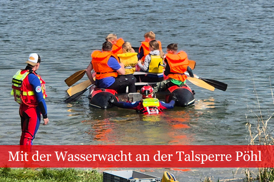 Mehrere Kinder und Jugendliche fahren im Schlauchboot auf einen See hinaus. begleitet werden sie von zwei Erwachsenen in Neoprenanzügen der Wasserwacht.