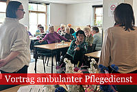 Mitglieder des Seniorenclubs sitzen an langen Tischen, die Mitarbeiterinnen des DRK stehen vor ihnen und halten einen Vortrag.