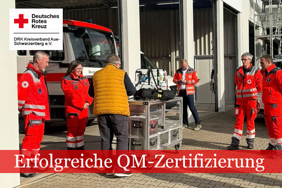Erfolgreiche QM-Zertifiziereun: Mehrere helfer in DRK-Einsatzkleidung und eine Person mit gelber Weste stehen vor einem DRK-LKW. Auf einem Wagen vor ihnen liegen verschiedene Metallkästen und Arbeitsgeräte.