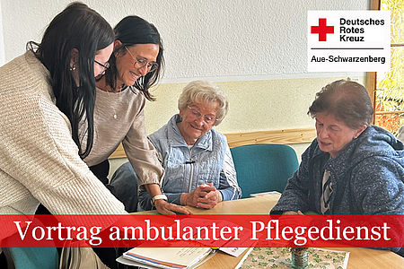 Beratungssituation: Zwei Frauen vom Seniorenclub sitzen am Tisch und schauen sich Unterlagen an. Zwei DRK Mitarbeiterinnen stehen am Tisch und schauen gemeinsam auf die Papiere.