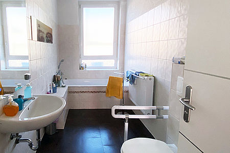 Gemeinschaftsbad mit Waschbecken Toilette und Badewanne im Hintergrund unter dem Fenster.
