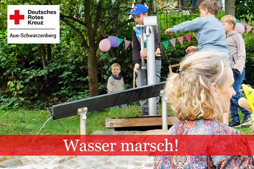 Kinder setzen an einer Pumpe einen Wasserlauf in Betrieb.